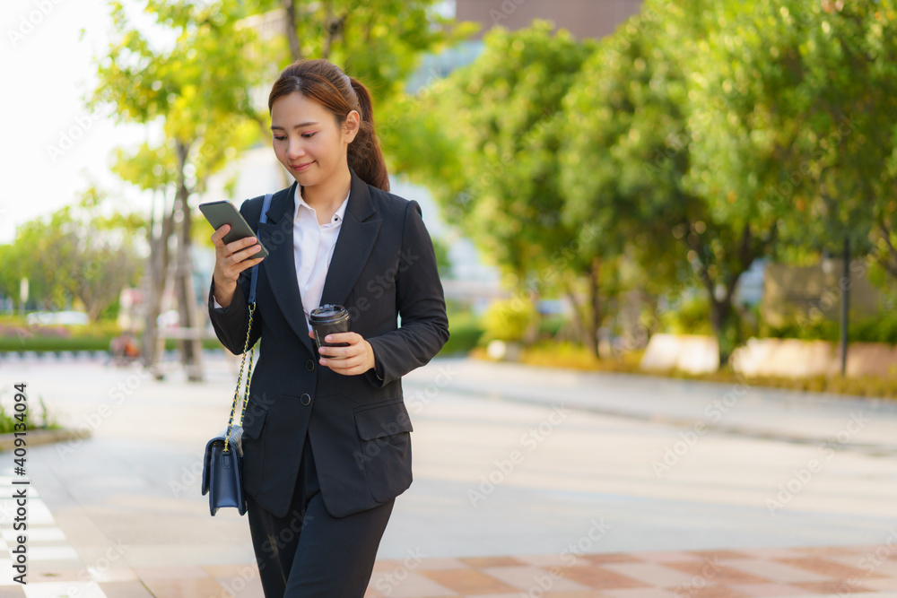 亚洲高管职场女性拿着咖啡杯在办公室的街道上使用手机