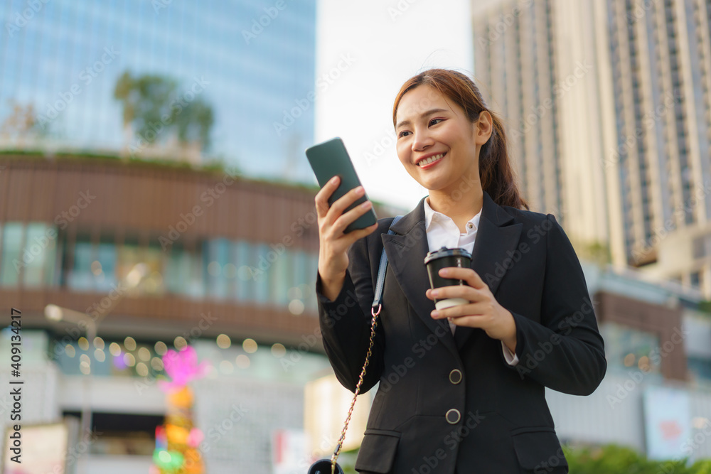 Asian executive working woman holding coffee cup and using a mobile phone in the street with office 