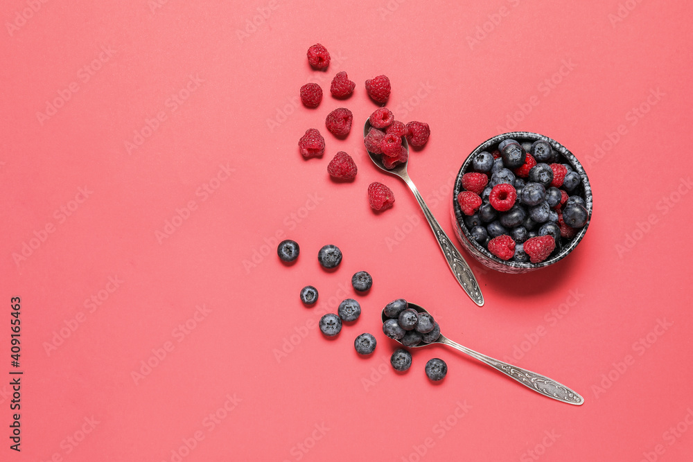 Bowl and spoons with different berries on color background