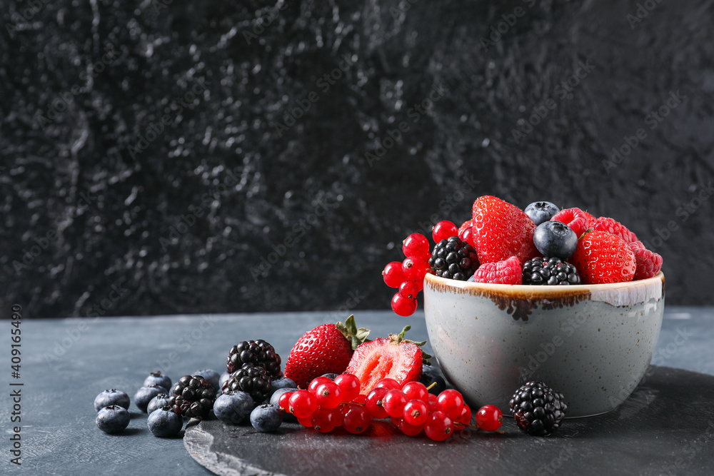 Bowl with different ripe berries on dark background