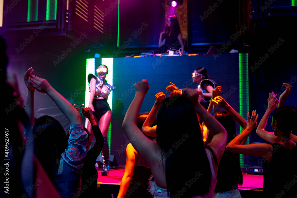 Group of people dance in disco night club to the beat of music from DJ on stage . New year night par