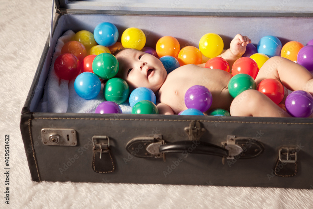 A baby lying down in the suitcase with color balls