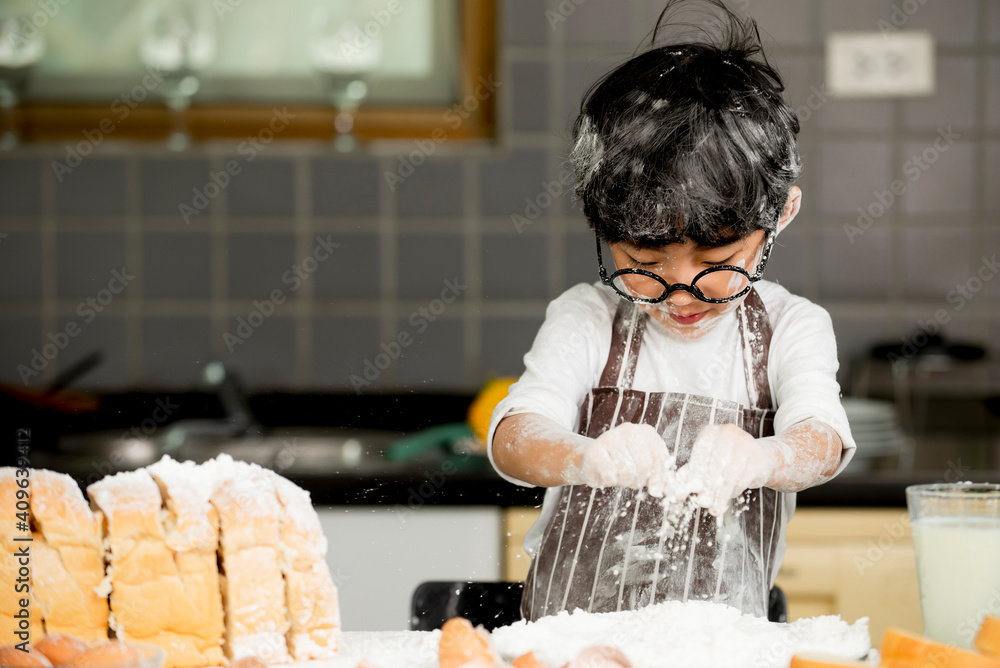 Happy cute asian  little boy in apron preparing baking the dough in kitchen room at home