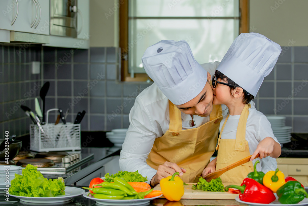 Cute asian little boy with  father  in uniform chef preparing cooking fresh salad in kitchen at home