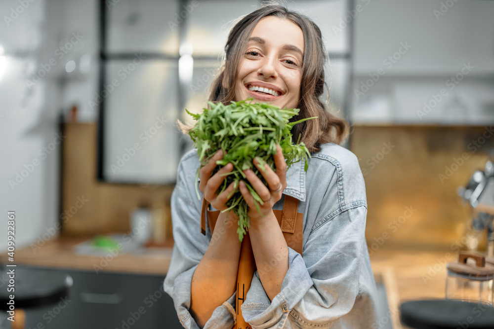 美丽微笑的女人穿着围裙，厨房里放着新鲜的芝麻菜。健康烹饪理念