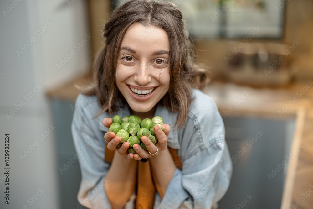 Portrait of pretty smiling woman with fresh brussels sprouts on the kitchen at home. Healthy cooking