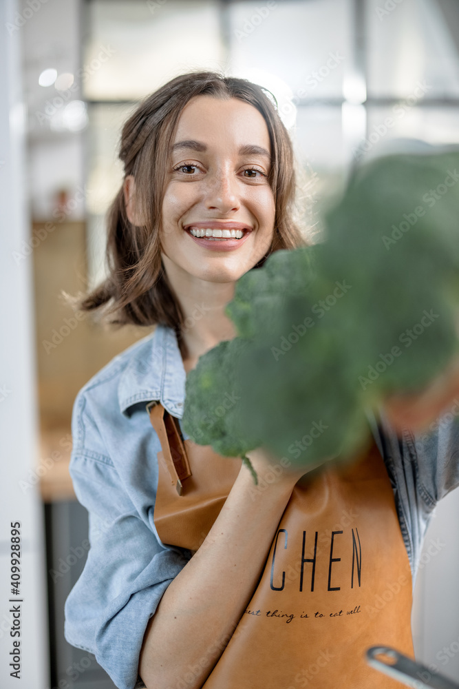 美丽微笑的女人穿着围裙，厨房里放着新鲜的西兰花。健康烹饪概念