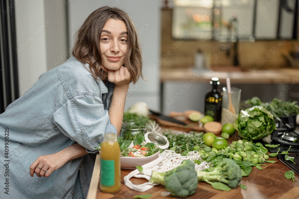 美丽的年轻女人在厨房里享用健康清洁的食物。吃绿色奶昔和沙拉配ve