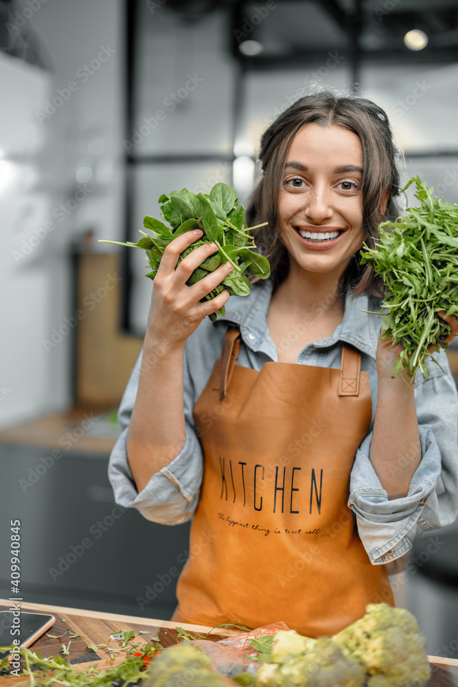 穿着围裙的快乐女人的画像，厨房里放着新鲜的菠菜和芝麻菜。健康烹饪c