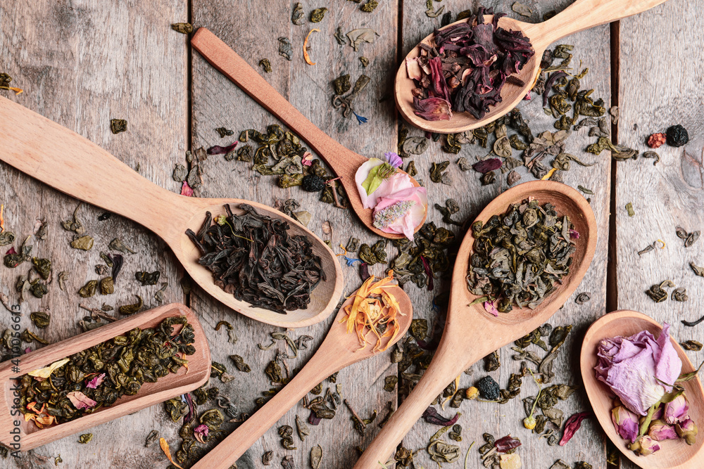 Spoons with different sorts of dry tea leaves on wooden background