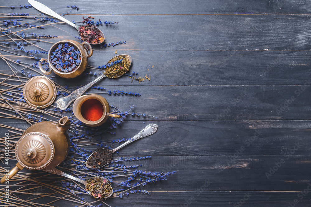 Teapot and spoons with different dry tea leaves on wooden background