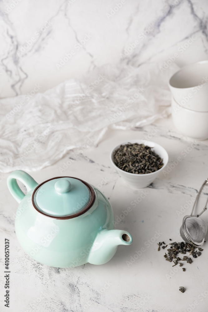 Composition with teapot and dry tea leaves in bowl on light background