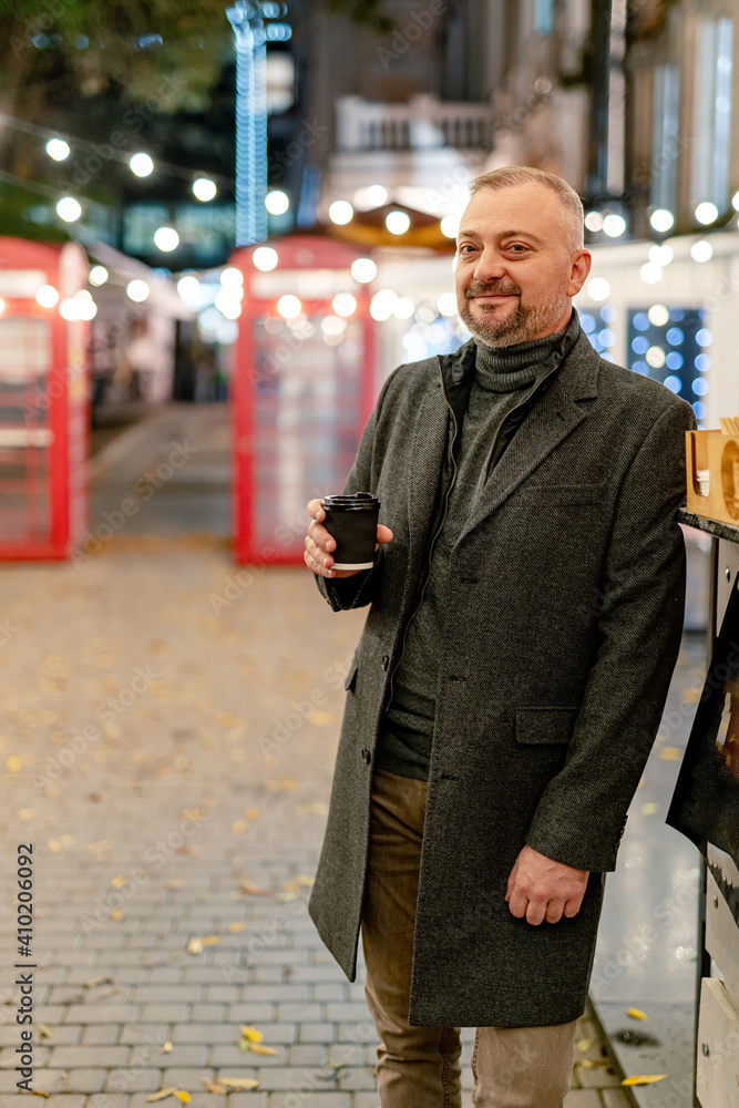 Half body portrait of a happy businessman standing outdoors with cup of coffee. Elegant coat and sui