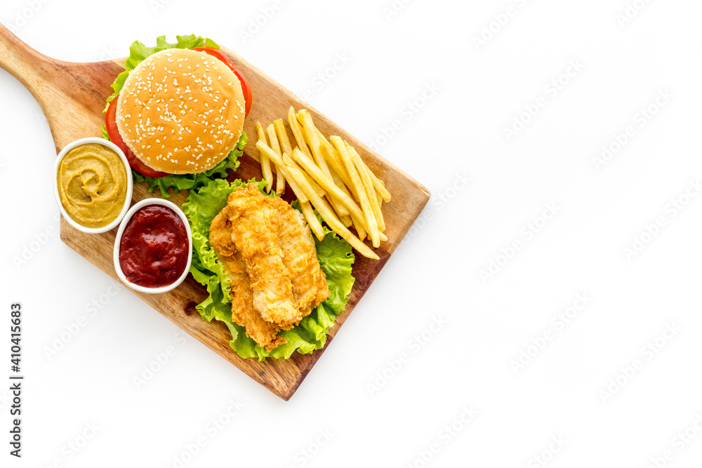 Burger served with french fries and fried chicken on wooden board. Top view