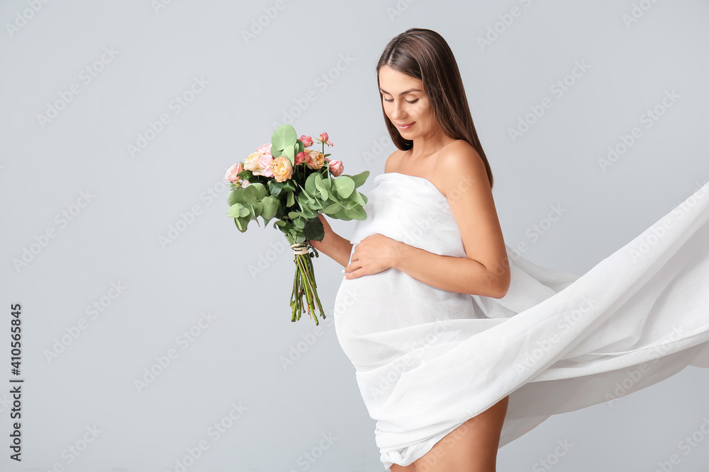 Beautiful pregnant woman with flowers on light background