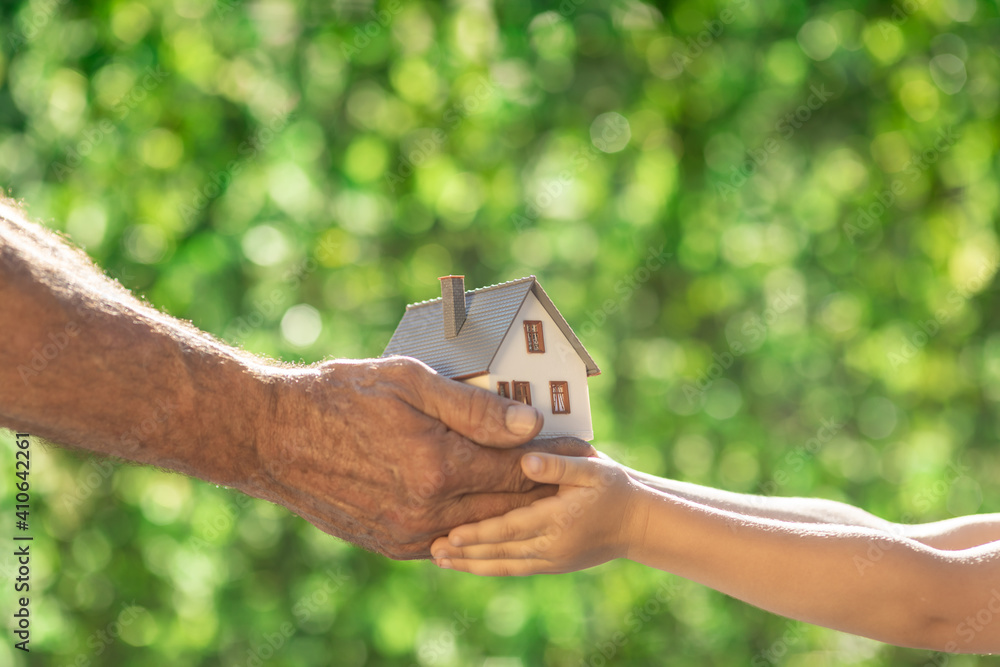 Family holding eco house in hands against spring green background