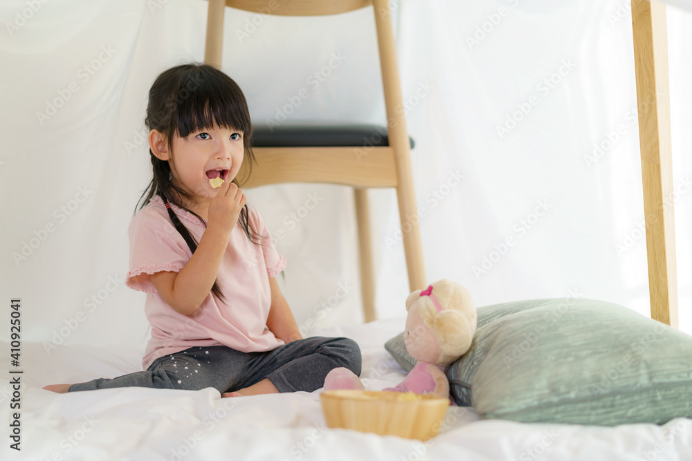 亚洲可爱的小女孩坐在家里客厅的毯子堡里吃零食