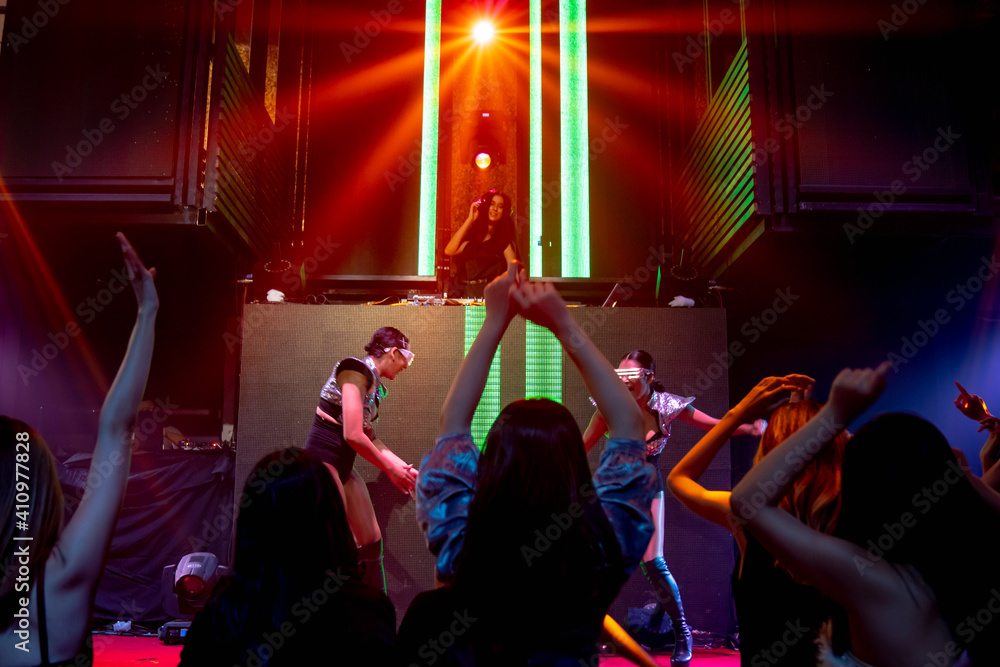 Group of people dance in disco night club to the beat of music from DJ on stage . New year night par