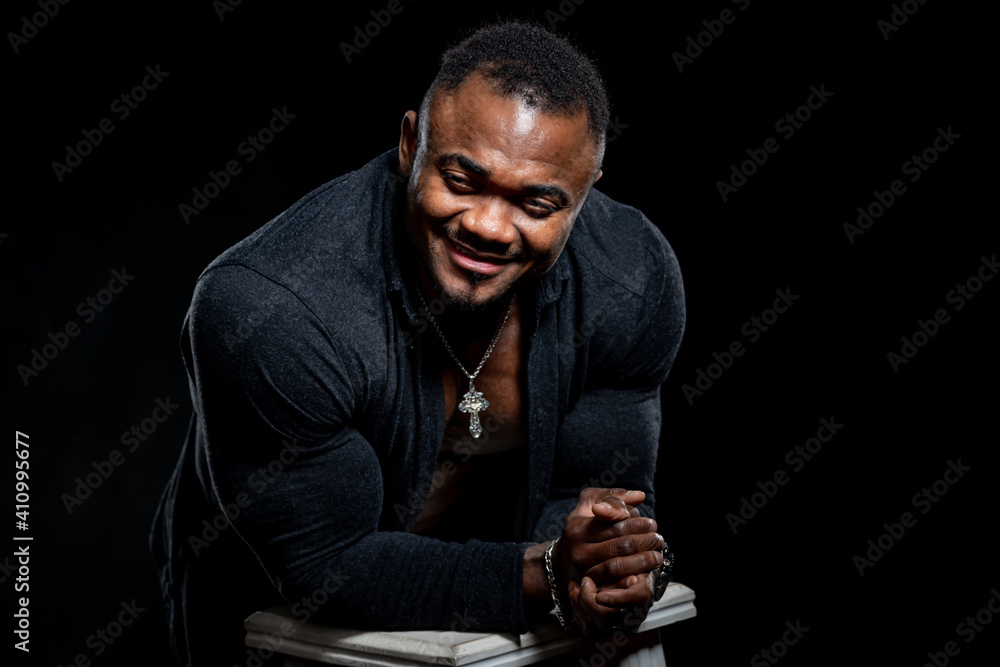 Handsome smiling muscular man in black shirt poses to the camera and leans on high bar chair with el