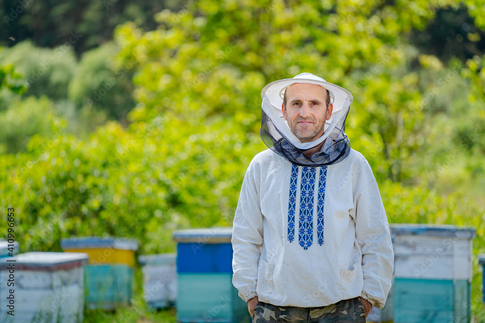 Owner of the apiary poses to the camera. Beekeeper stands with hands in pockets stands on colorful h