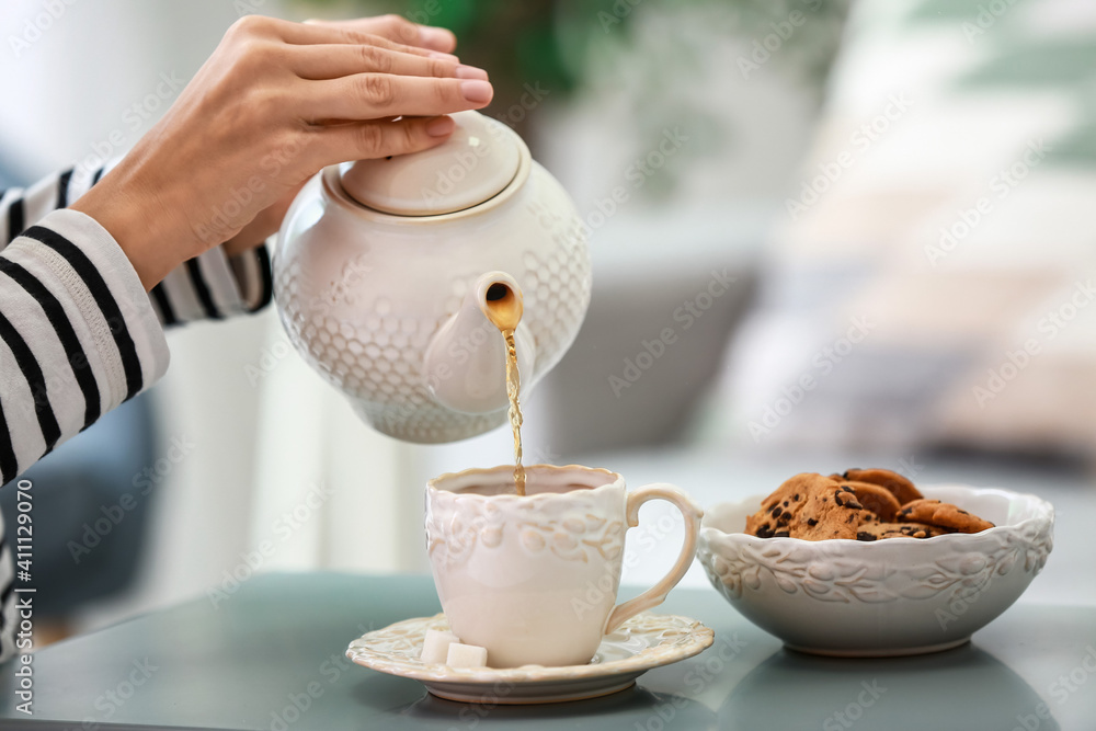 Woman pouring hot tea from teapot into cup at table