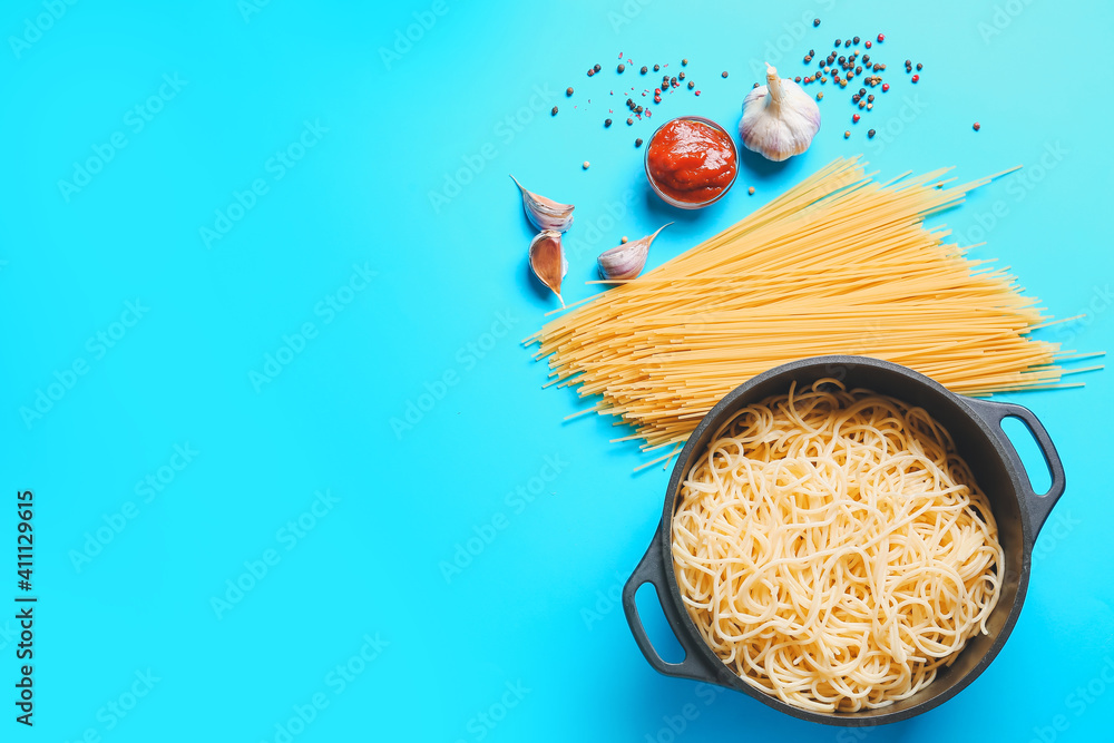 Cooking pot with pasta and ingredients on color background