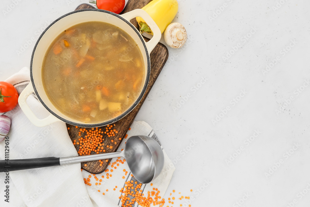 Cooking pot with tasty soup and vegetables on light background