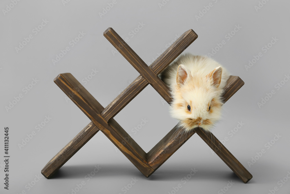 Cute fluffy rabbit and decorative stand on grey background