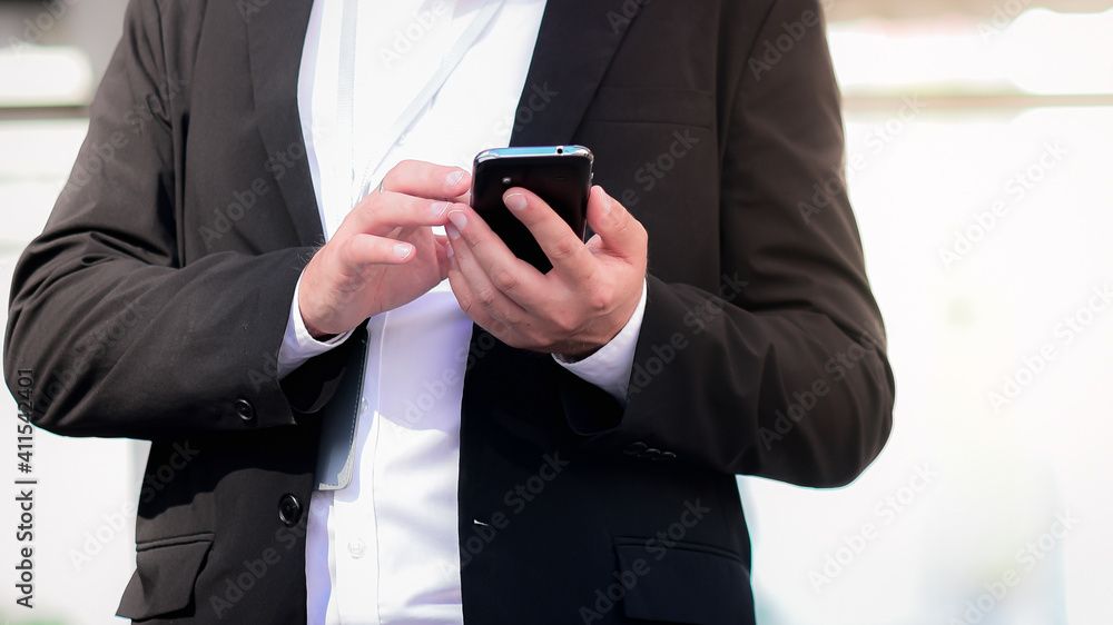 Urban smart caucasian businessman age 30-40 years old In a dark suit standing and using a smartphone