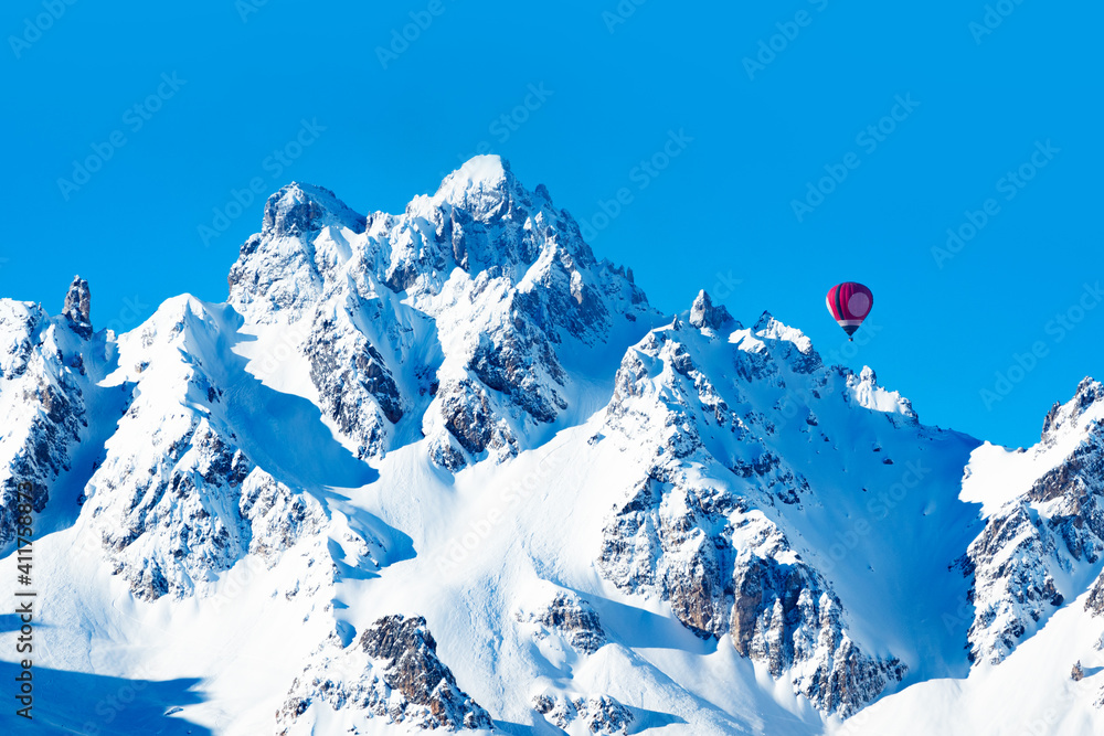 Colorful hot air balloon over high French Alps mountain peaks on sunny day