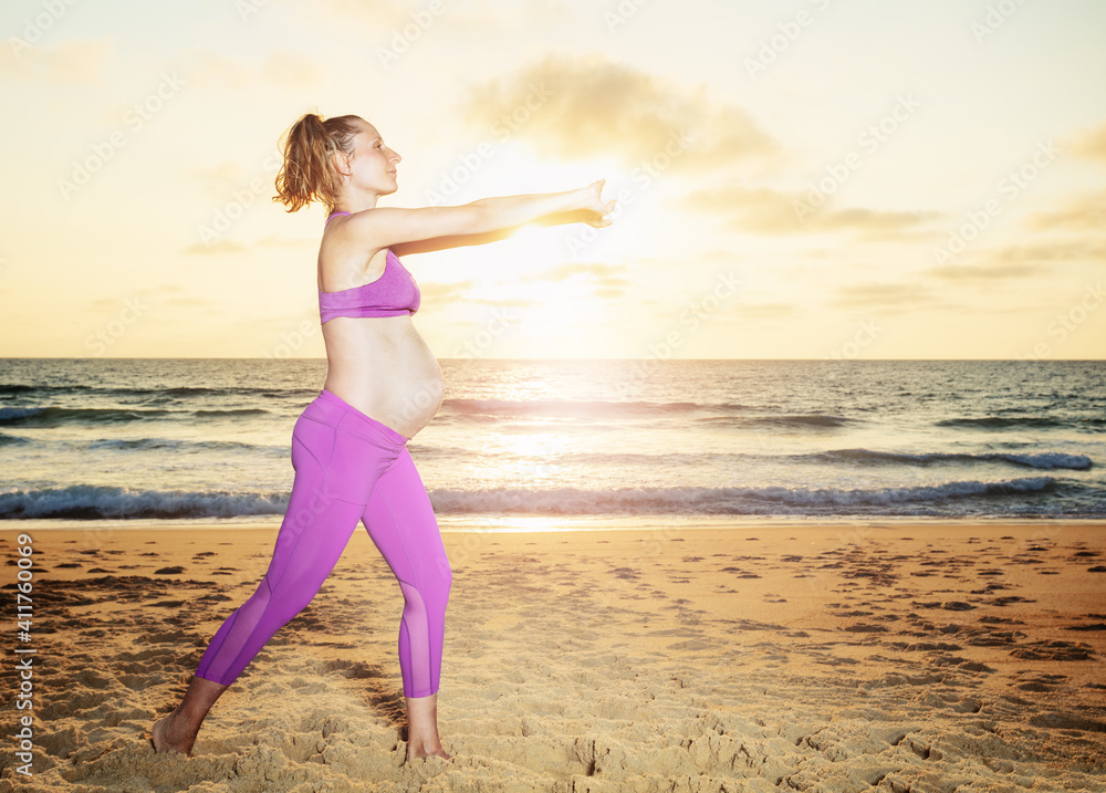 Pregnant woman exercise on the sand beach with sunset over ocean on background