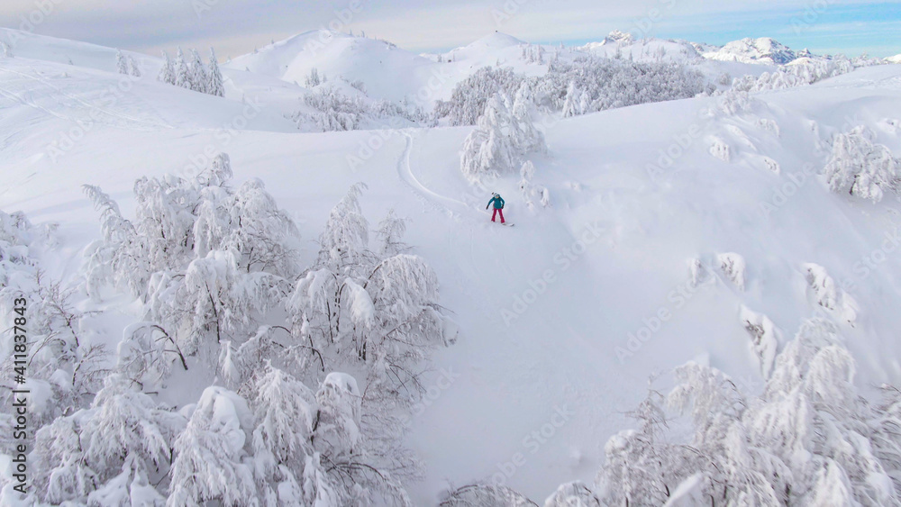 空中：在朱利安阿尔卑斯山的雪山上，一名单板滑雪运动员从上方飞过