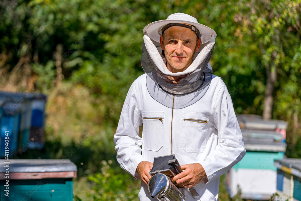 Beekeeper in the sunset surrounded with bees holds beesmoker in hands. Half body portrait of a man i