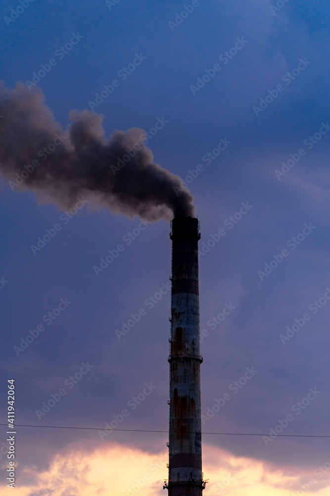 古老的、风化的、高大的工业工厂烟囱，上面有烟雾。多云的天空背景。