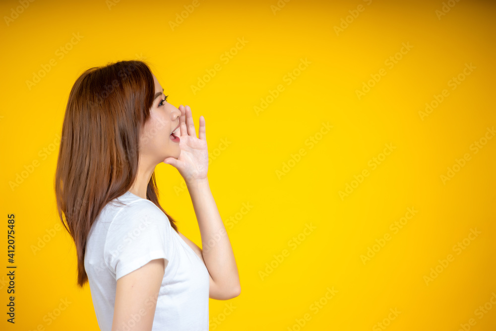 Young Asian woman in white casual t-shirt looking aside, shouting or annoucing something over yellow