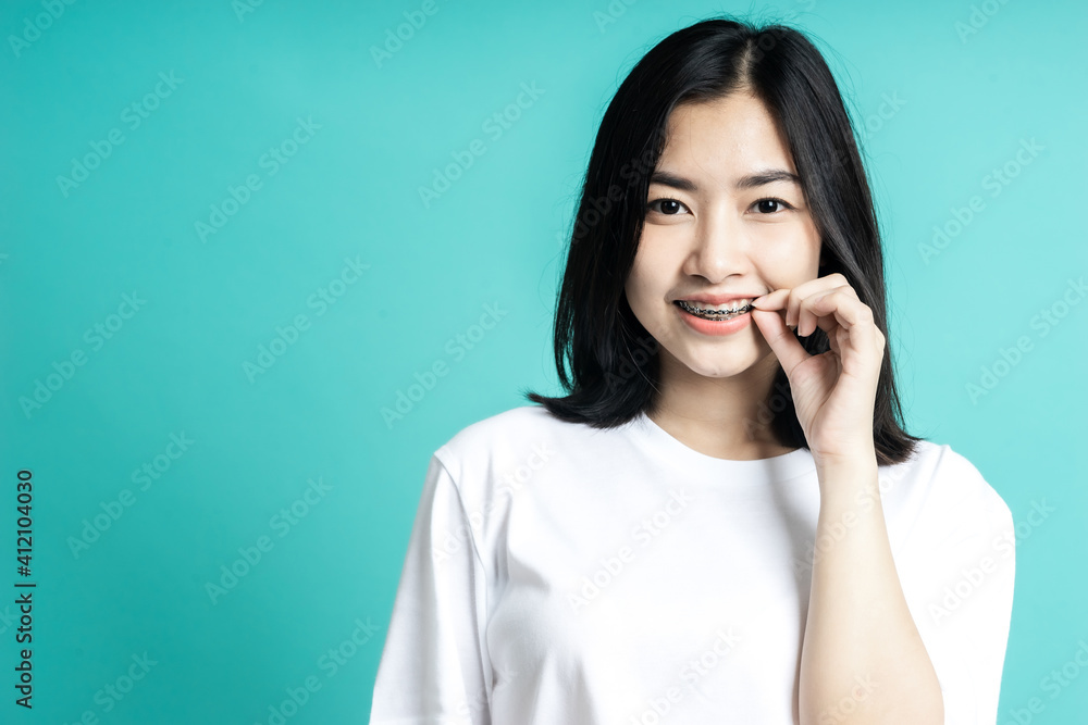 Asian woman wearing dental braces pointing to tooth sample and smiling with her healthy white teeth 