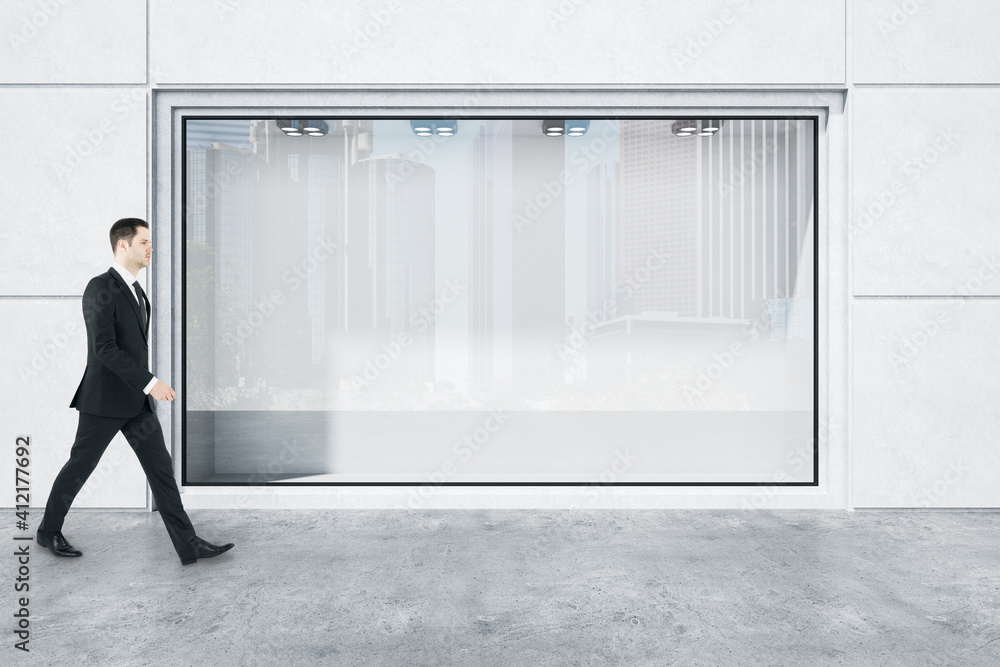 Businessman in black suit goes by huge street shop window with city reflection in modern concrete st