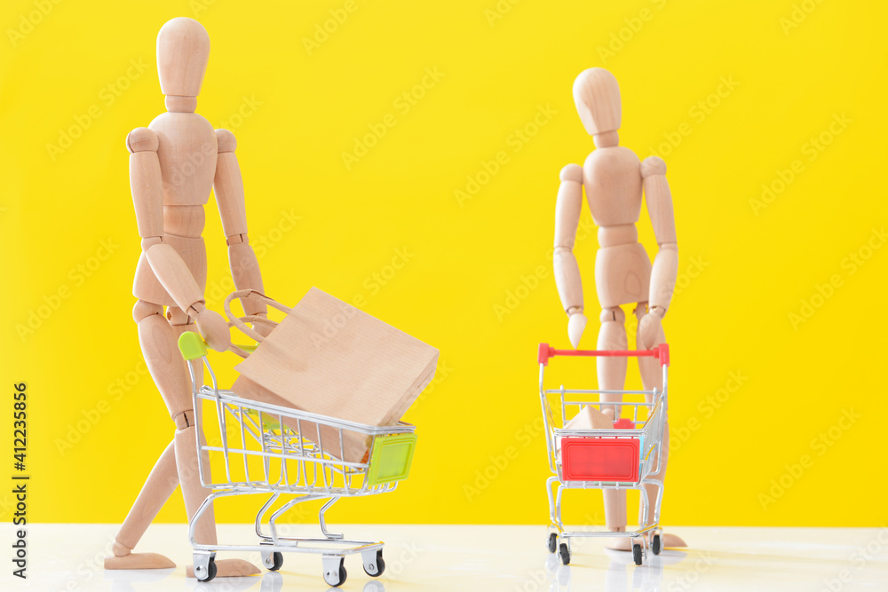 Wooden mannequins with shopping carts on color background