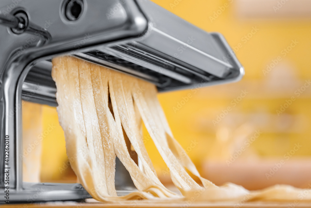 Pasta maker with dough on table in kitchen, closeup