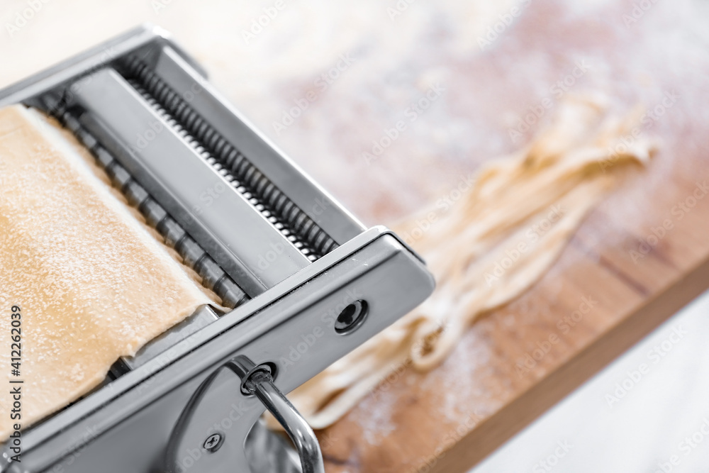 Pasta maker with dough on table in kitchen