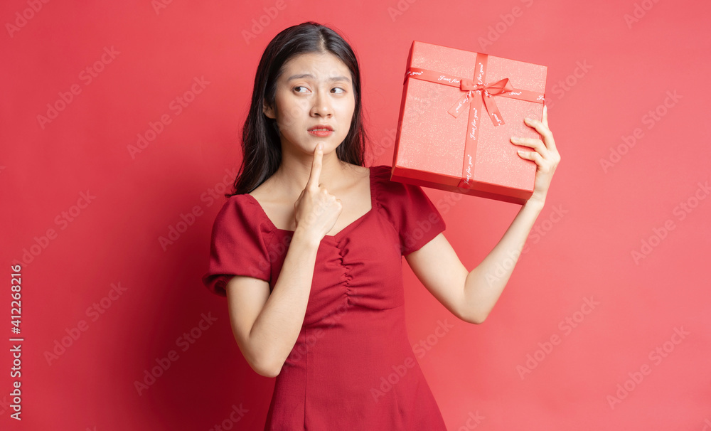 Asian young girl in dress holding red gift box with cheerful expression on background