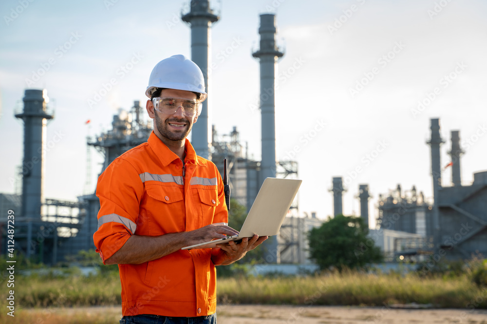 Refinery industry engineer working on computer laptop against oil refinery background.