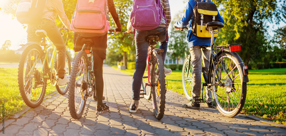 Children with rucksacks riding on bikes in the park near school