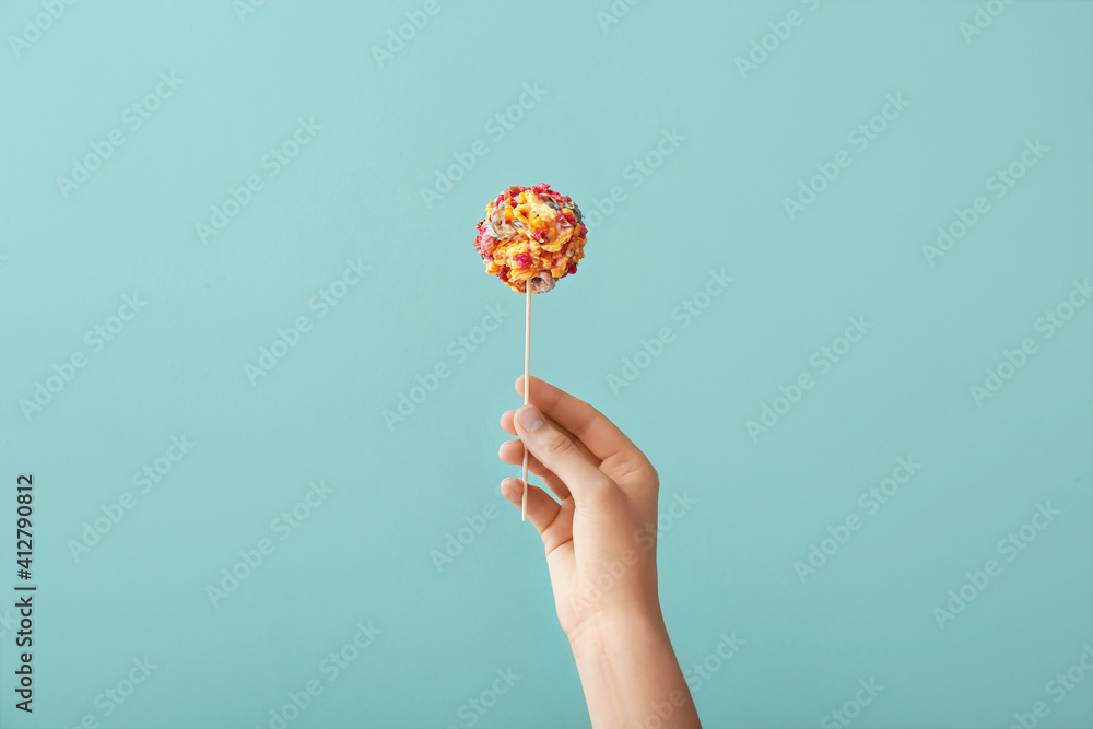 Woman holding tasty popcorn ball on color background