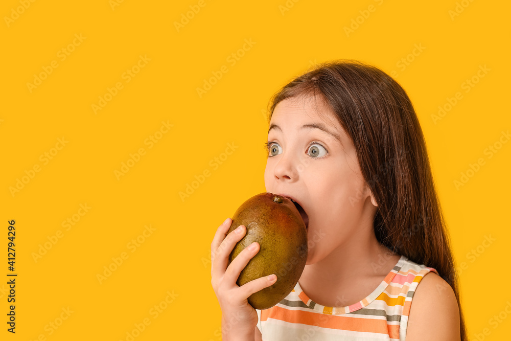 Surprised little girl eating tasty mango on color background