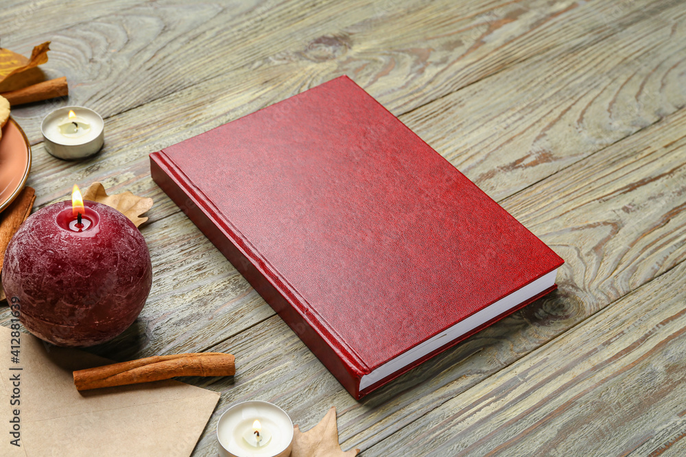 Blank book, autumn leaves and candles on wooden background