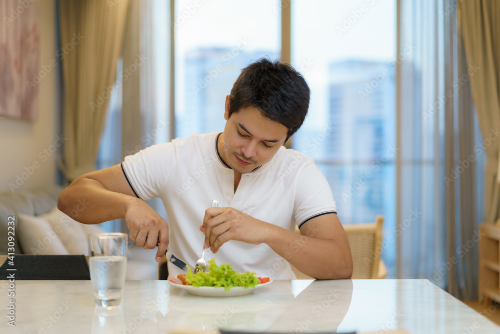 一名亚裔男子正在家中客厅吃美式早餐。