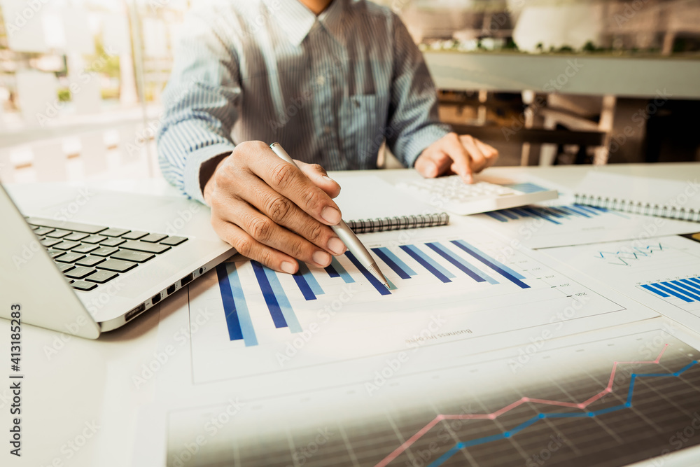 Businessmen are analyzing business graphs on their desks and calculating them using a calculator. Fi