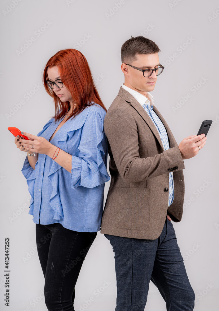 Full length photo of a young casual couple standing back to back and looking at phone screens. Peopl