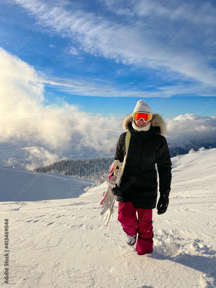 CLOSE UP Smiling young woman hikes up an ungroomed hill during snowboarding trip